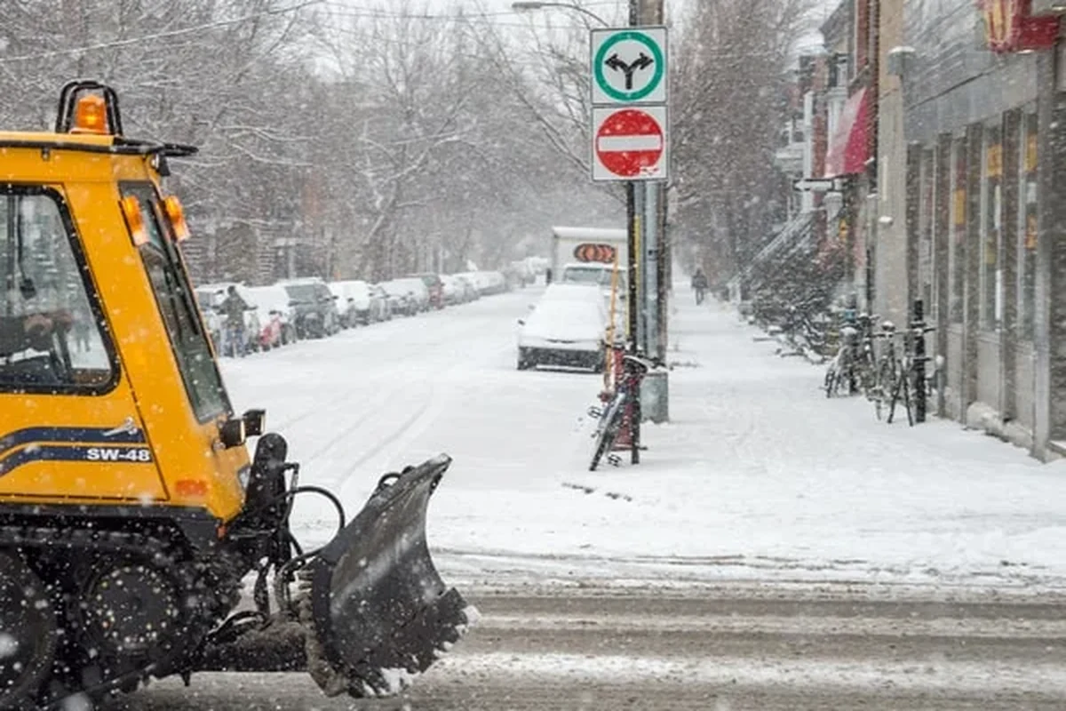 Tracked snow plow clearing a commercial street during an active snowstorm