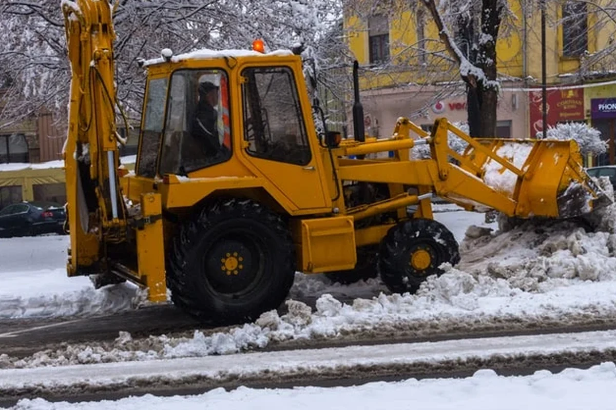 Backhoe loader clearing snow from a commercial street during winter service