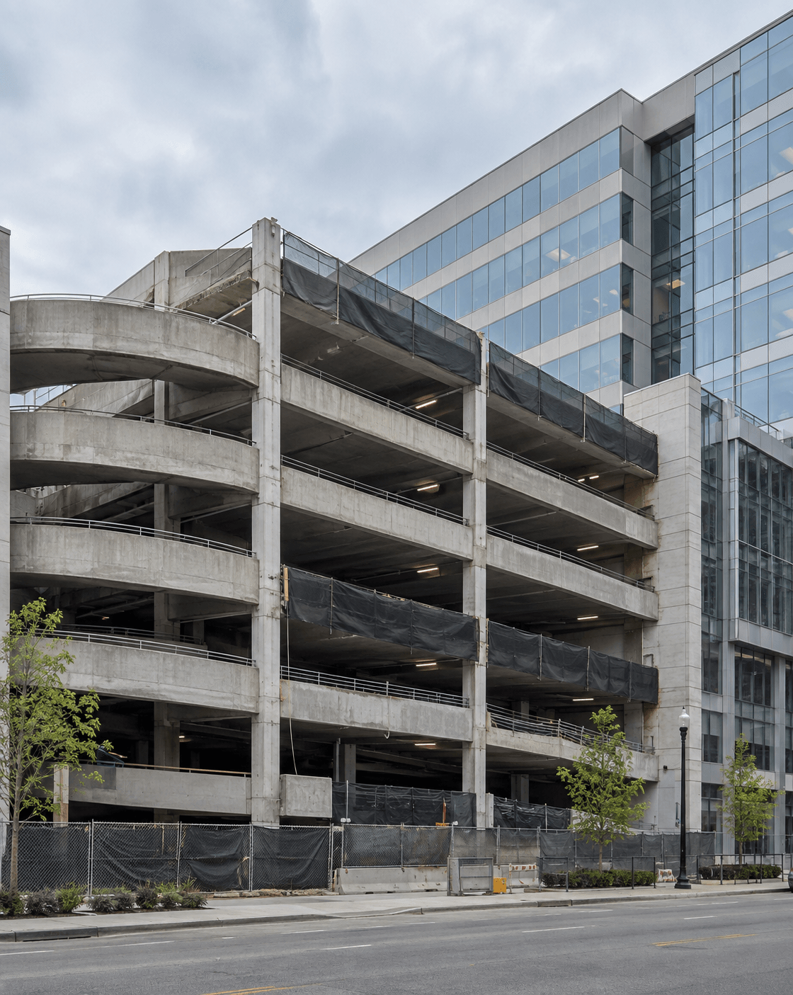 Commercial podium parking garage with multi-level concrete decks and ramps attached to a mid-rise office building before structural teardown — parking structure demolition scope