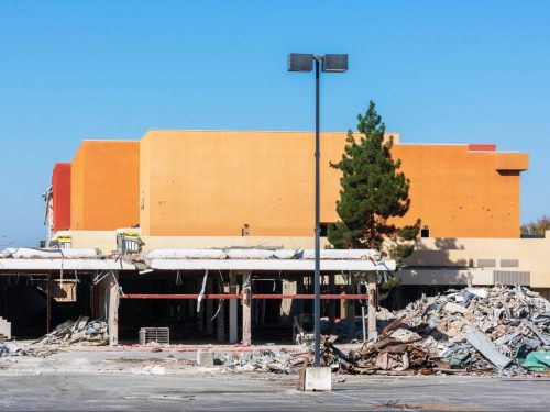 Partially demolished large commercial business property with exposed lower floor. Pile of demolition construction debris is ready for haul away service.